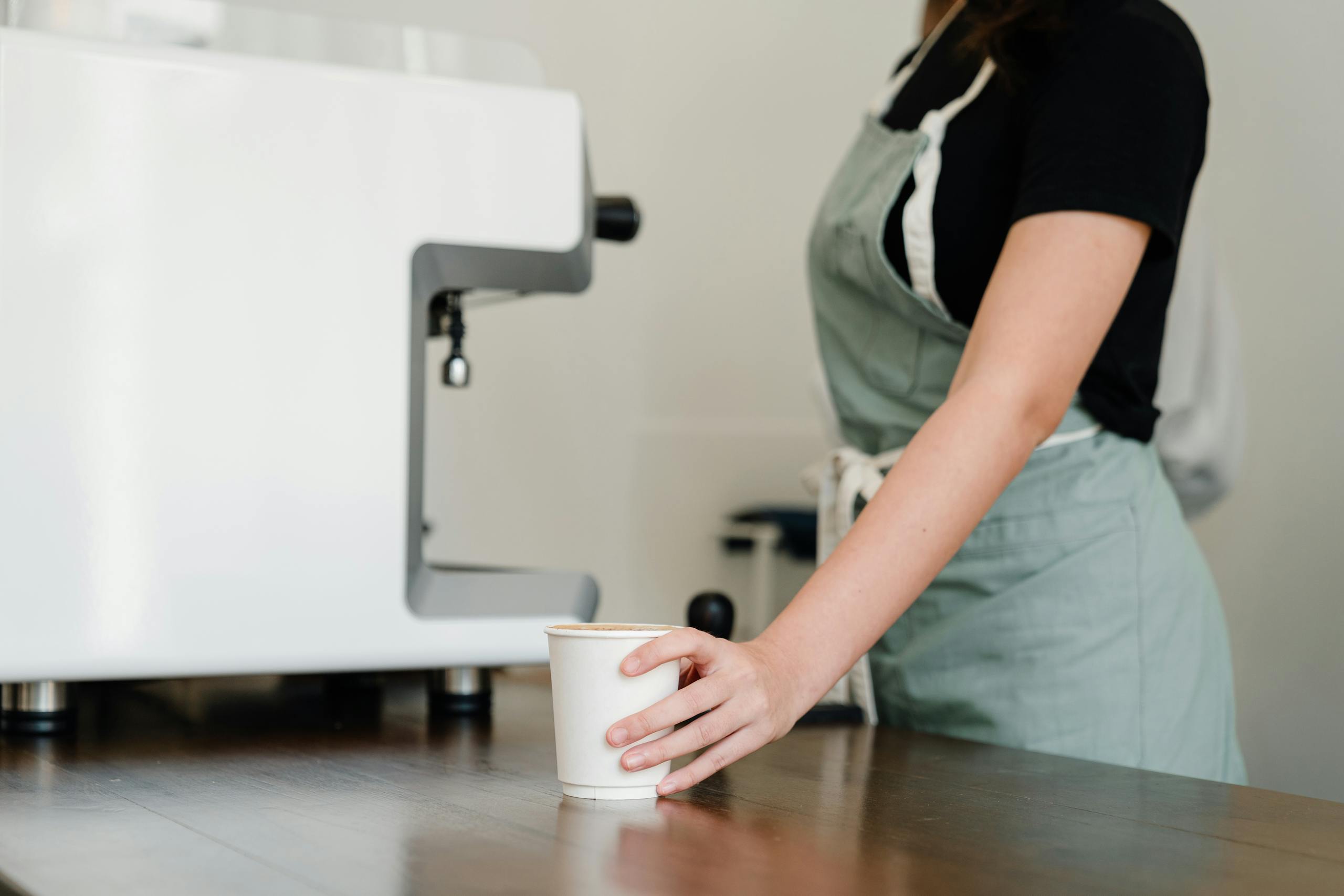 A barista in an apron serves coffee from a machine at a café.