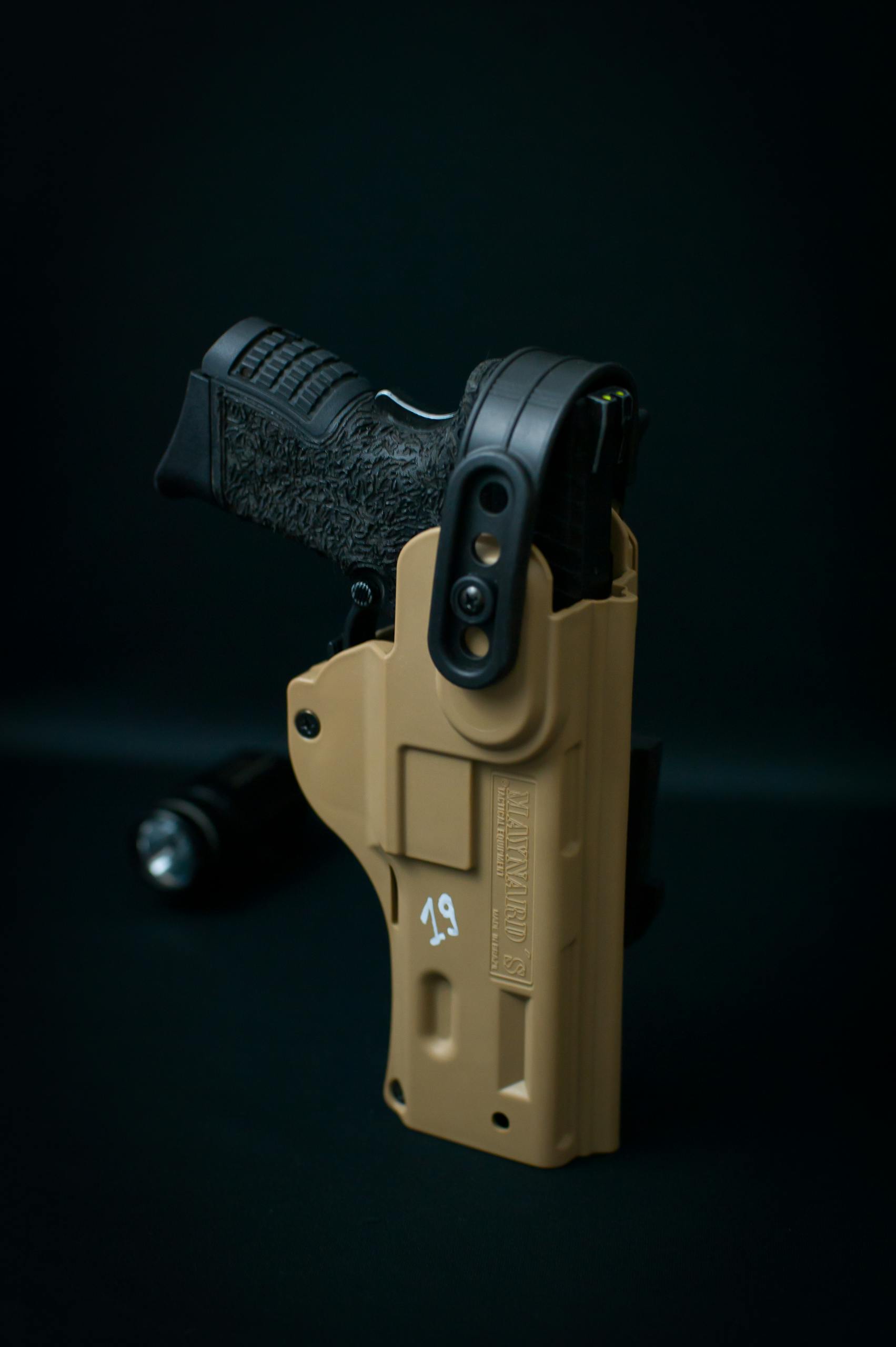 Close-up shot of a black handgun secured in a tan holster, against a dark background.