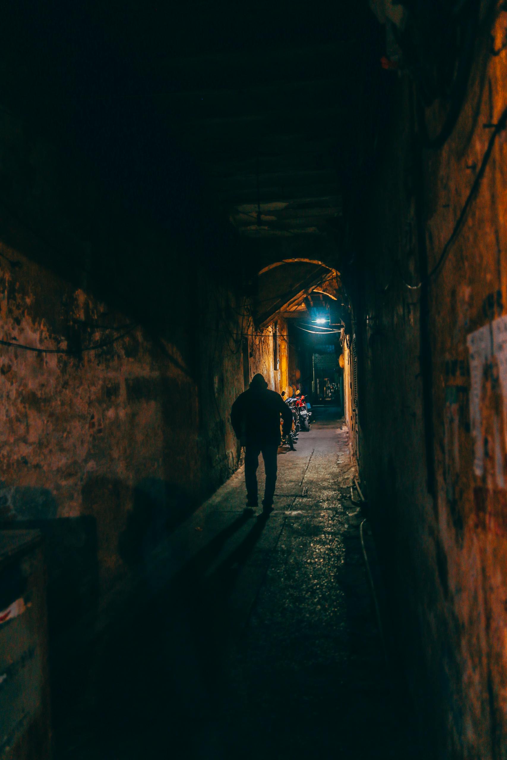 Silhouette of a person walking through a dimly lit alley in Hoàn Kiếm, Hanoi at night.