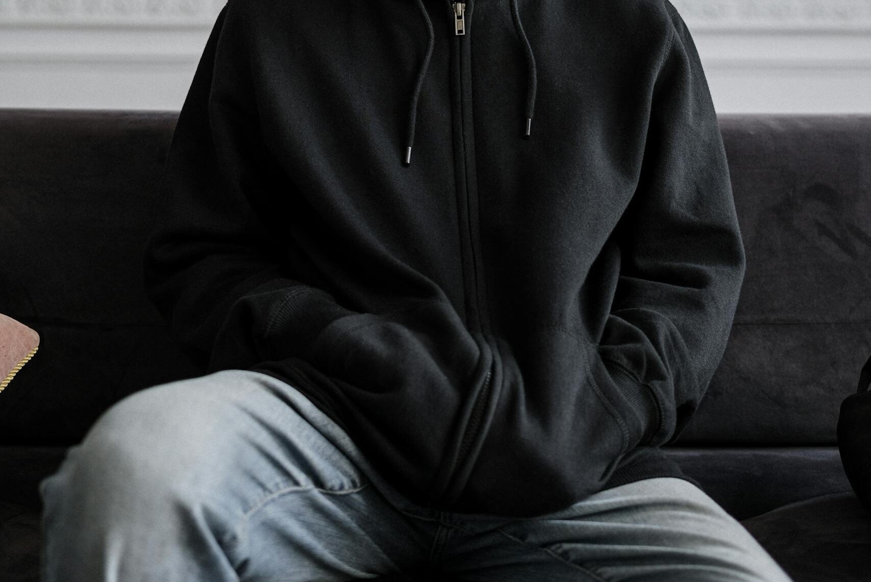 Teenager in a black hoodie sitting on a couch, reflecting on thoughts indoors.